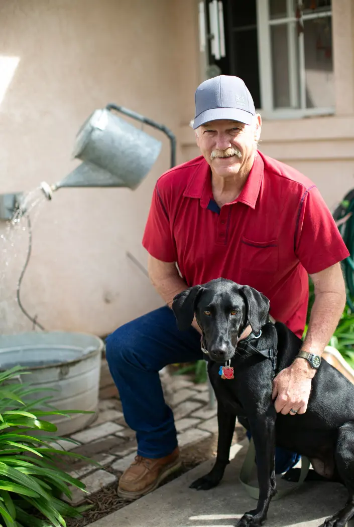 Mike Stevens, Home renovation expert, with his black lab, Kacie. Standing in front of a custom watering can fountain.